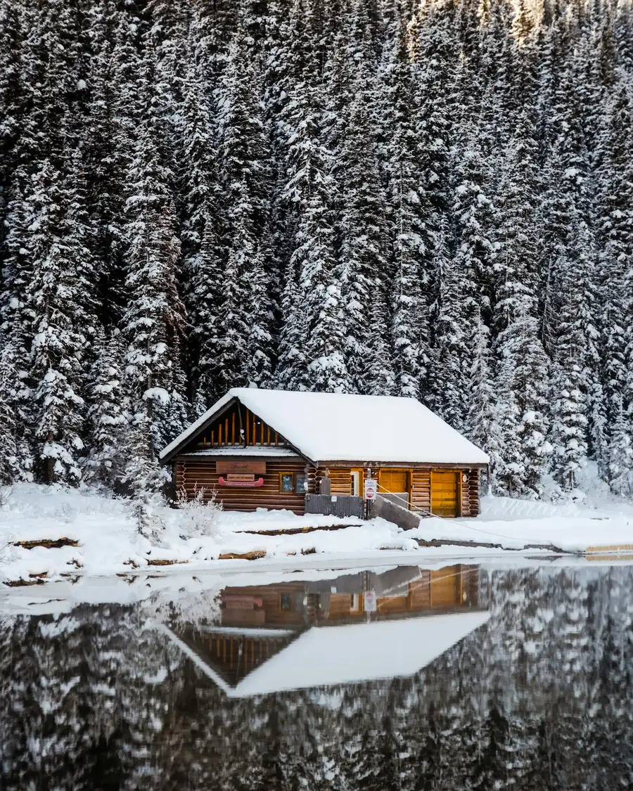 Log cabin reflected in a still lake in front of snowy spruces