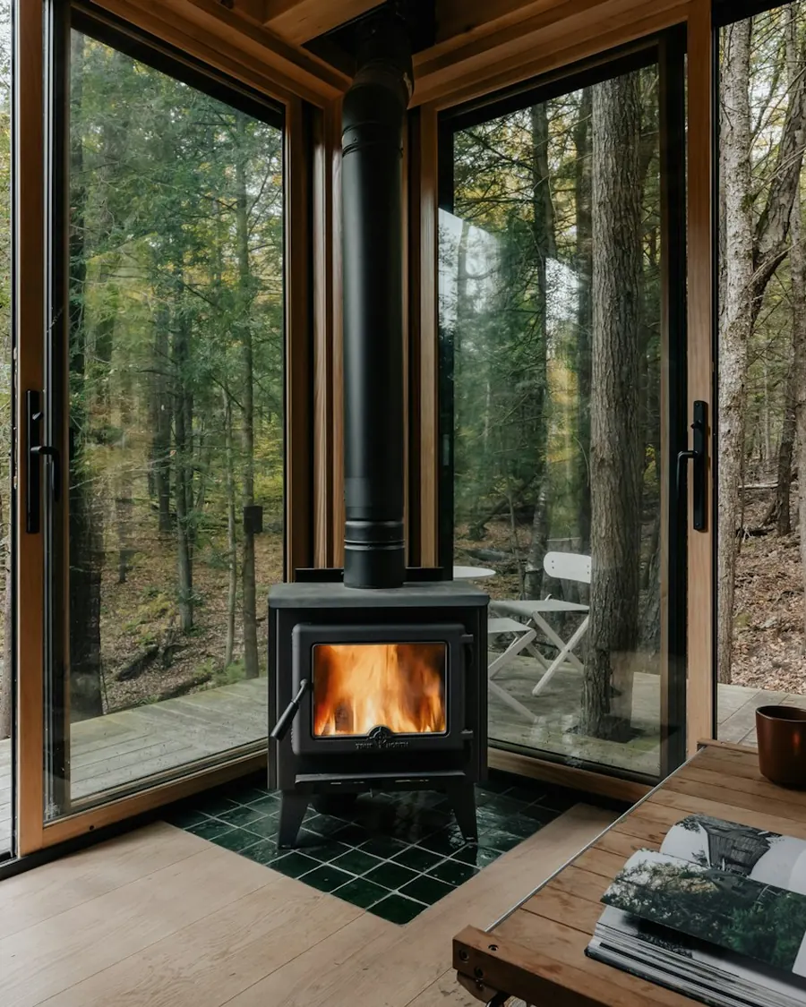 Wood stove burning in a glass walled lounge with windows onto the forest