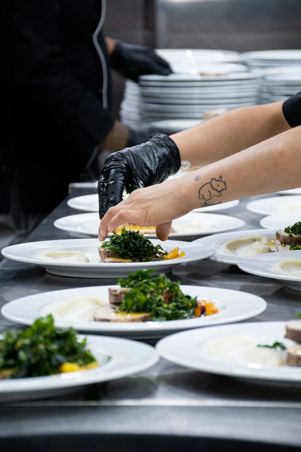 A gloved cook garnishing plates on the pass