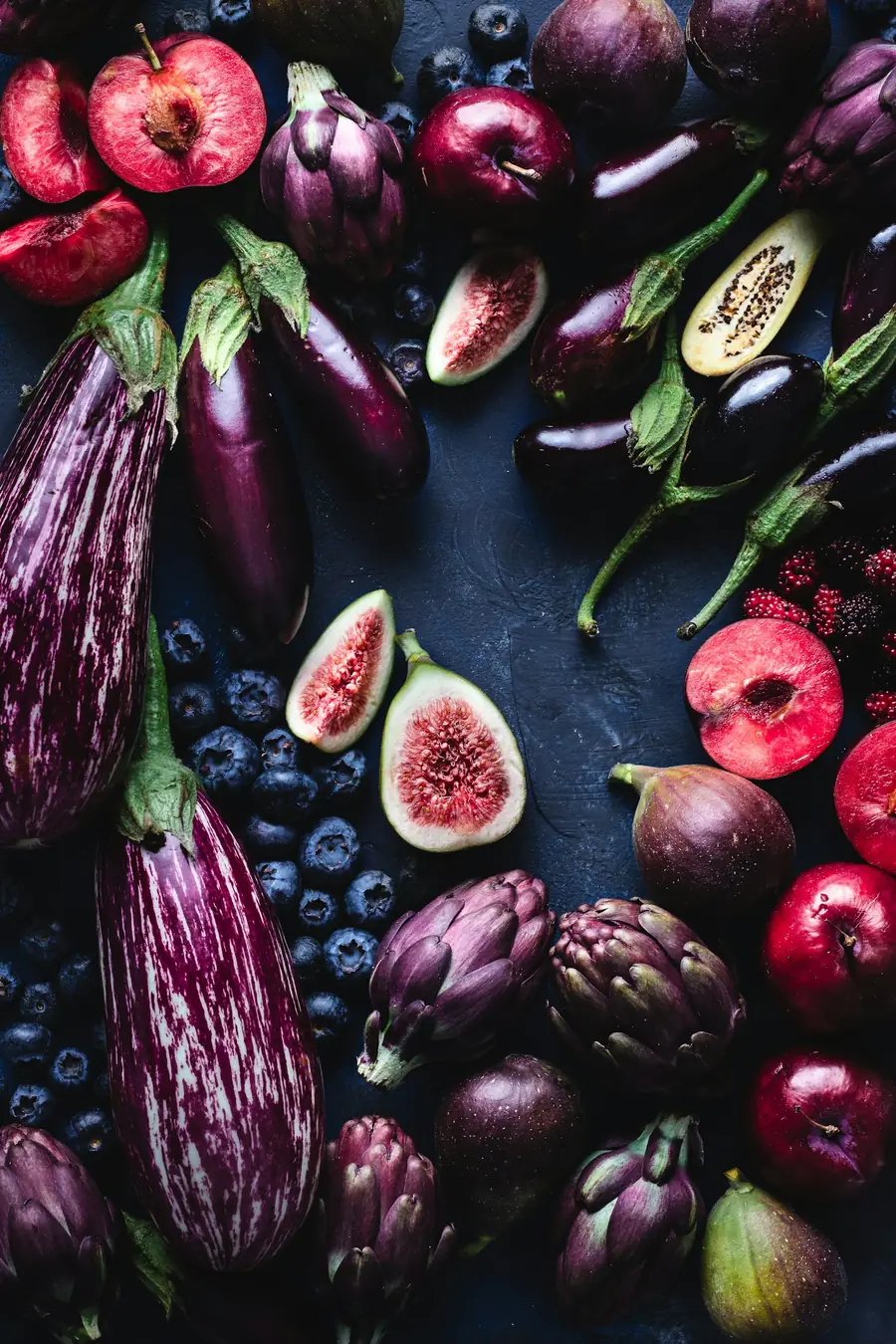 Figs, aubergines, artichokes and berries on a dark surface