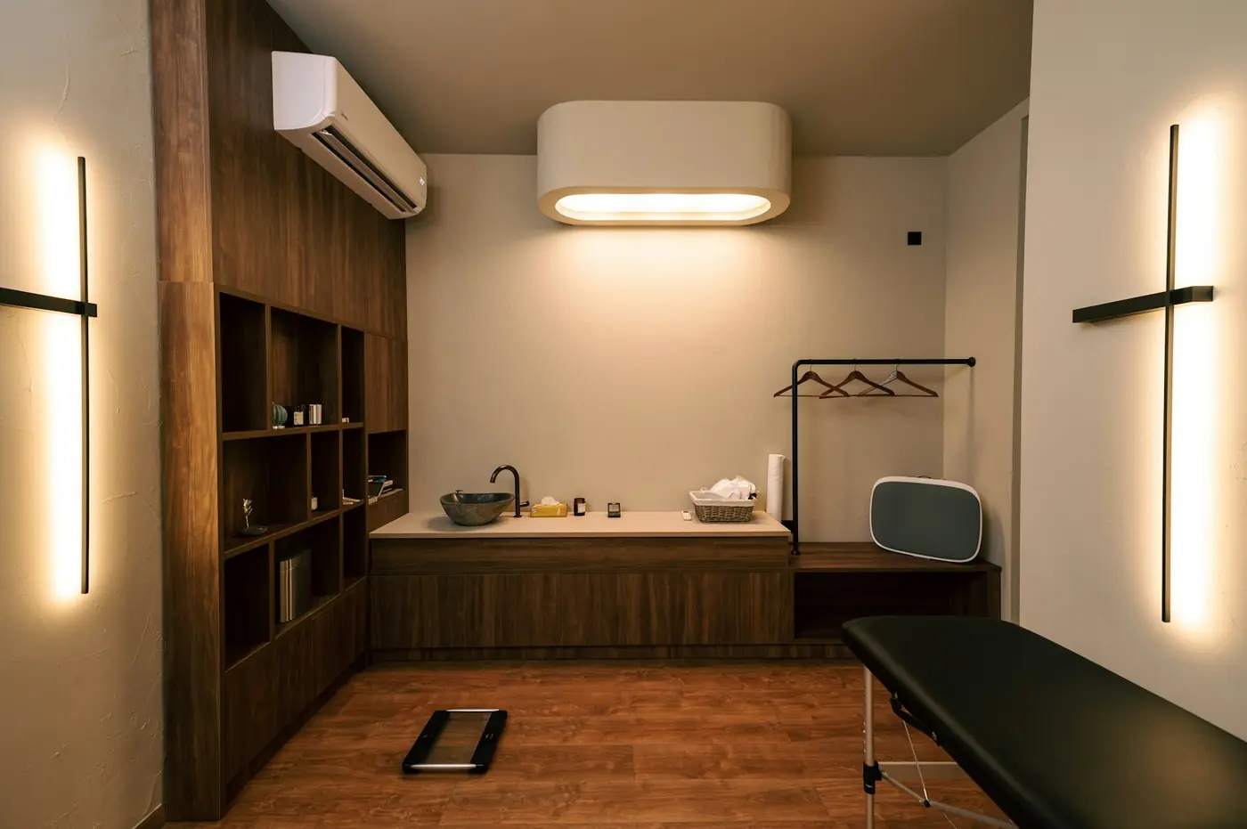 A calm consulting room with walnut cabinetry, warm light and an examination couch