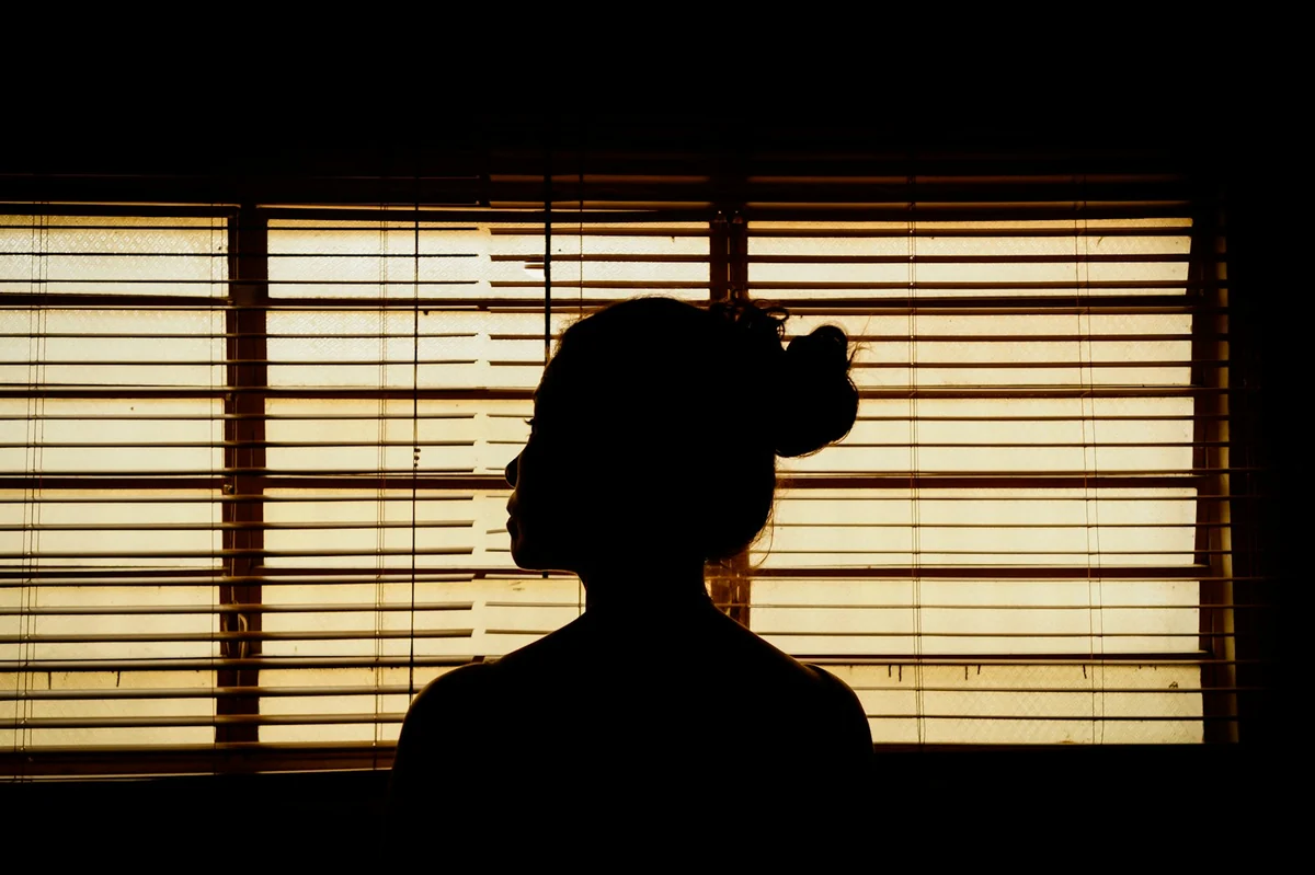 Silhouette of a person sitting in front of blinds with warm light coming through