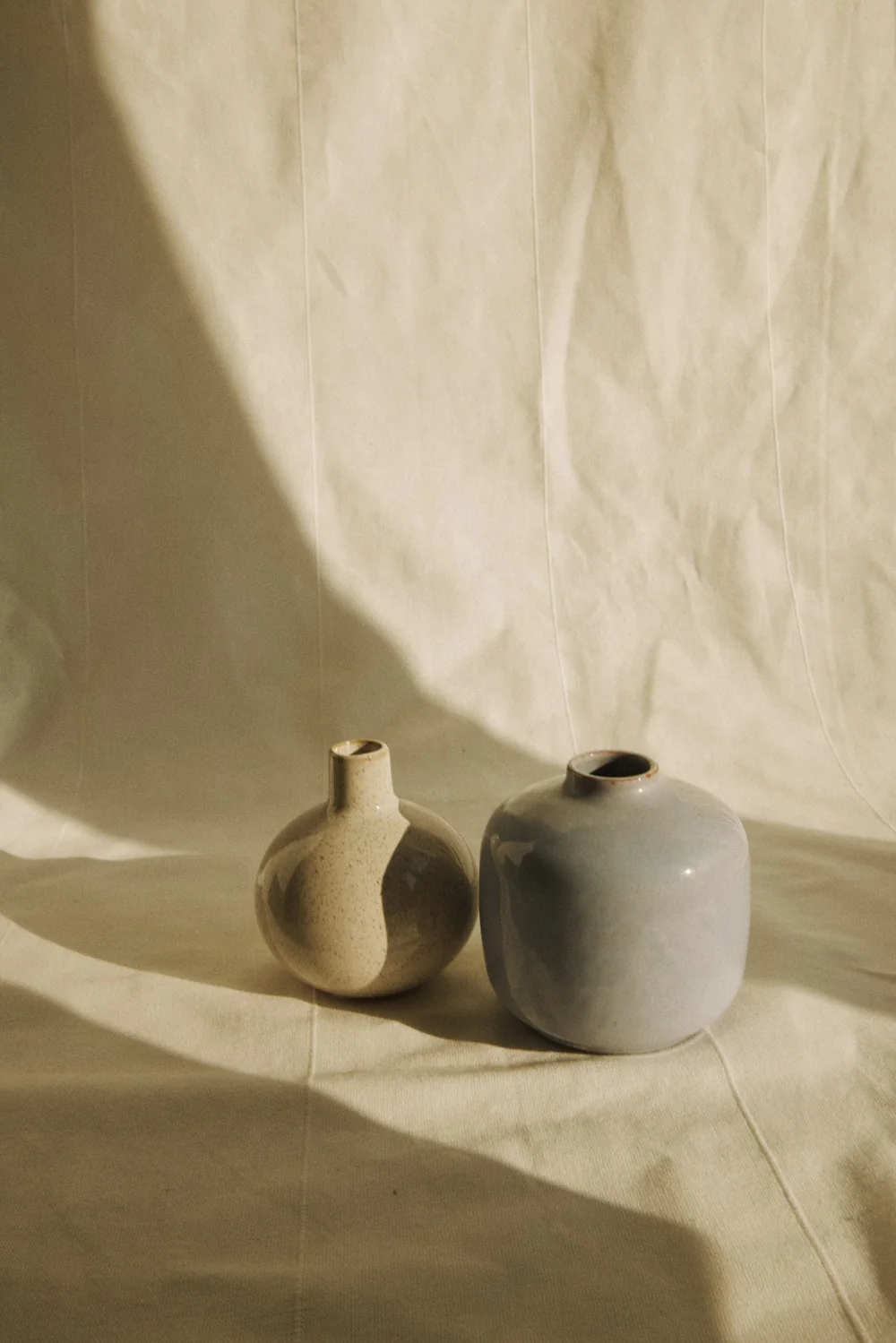 Two small ceramic vases standing side by side on linen cloth