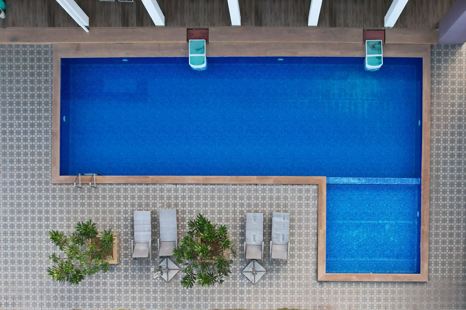 Draufsicht auf ein L förmiges Becken mit blauem Mosaik, Flachwasserbereich und gemustertem Steinboden