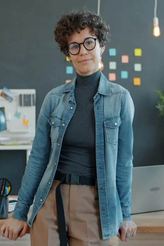 Eine lächelnde Frau mit Brille lehnt in einem Büro an ihrem Schreibtisch