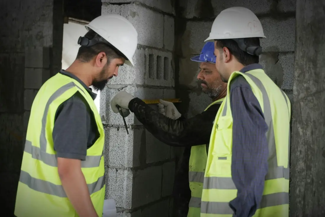 Baretli üç çalışan bir duvarın ölçüsünü birlikte kontrol ediyor