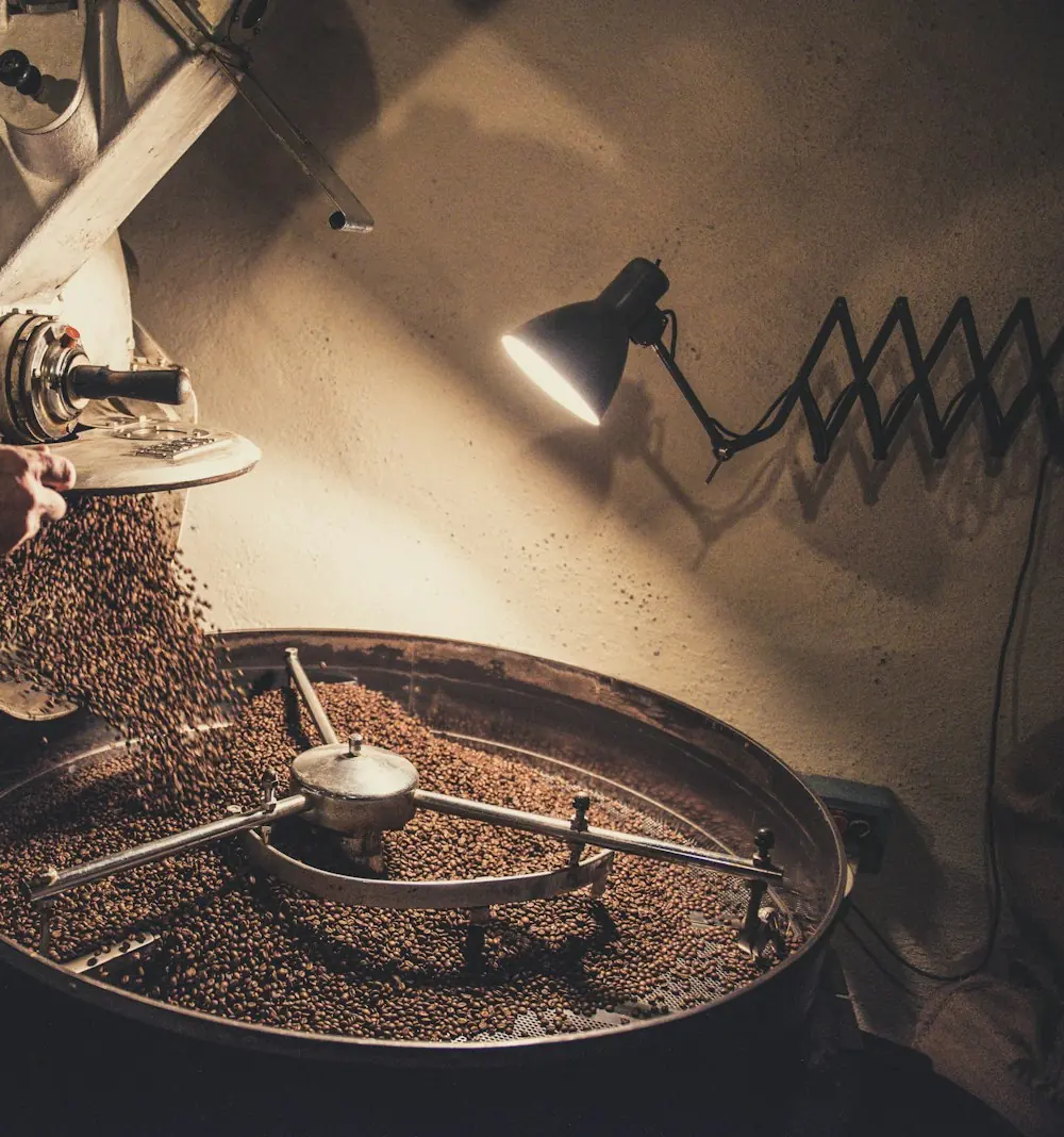 Beans pouring from the roasting drum into the cooling tray in dim workshop light