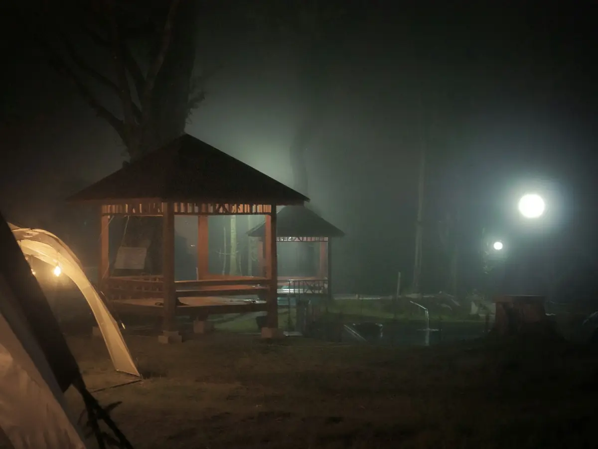 Beleuchtete Holzpavillons und ein Zelt in einer nebligen Nacht