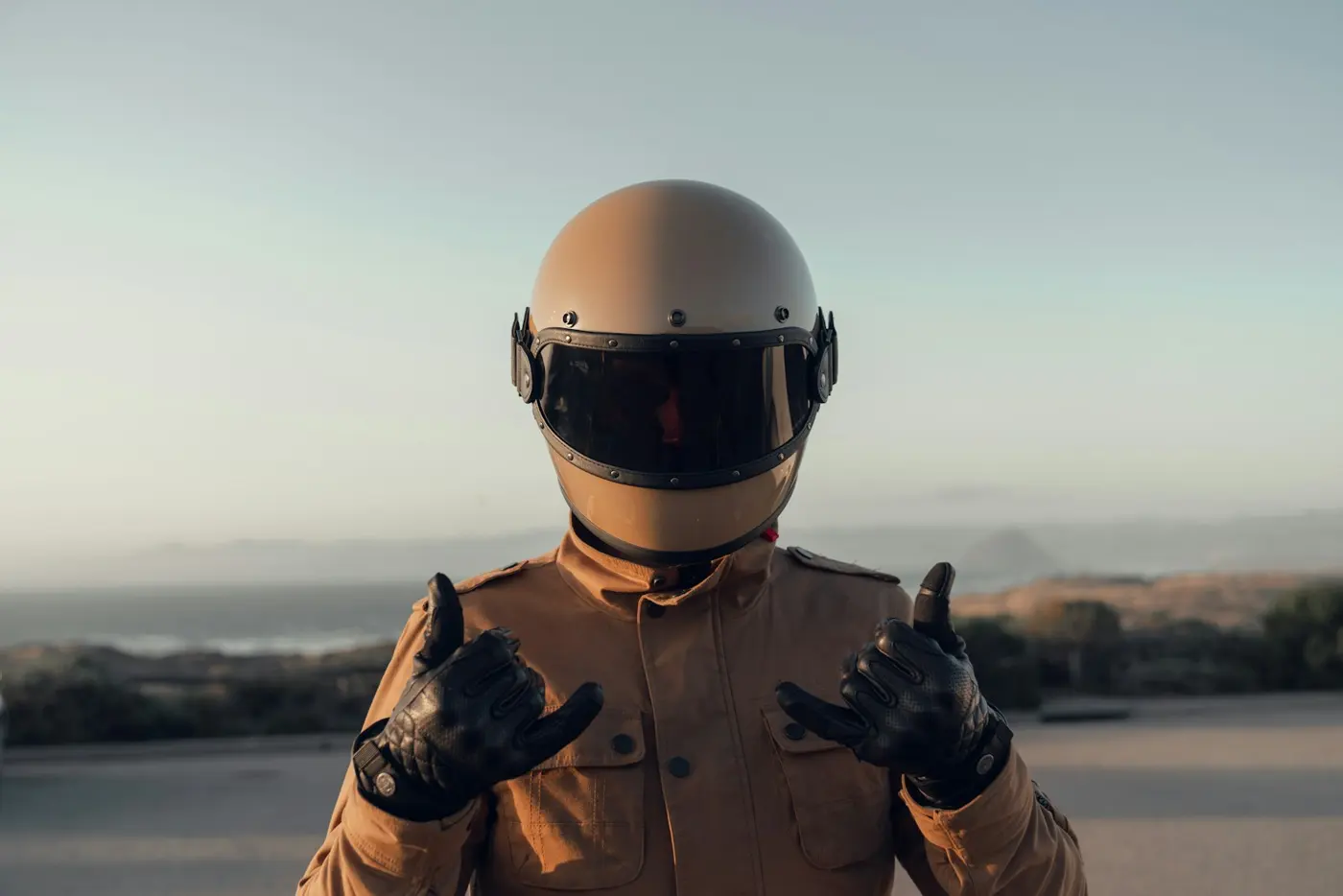 Rider by the sea in a beige helmet, tan riding jacket and black leather gloves
