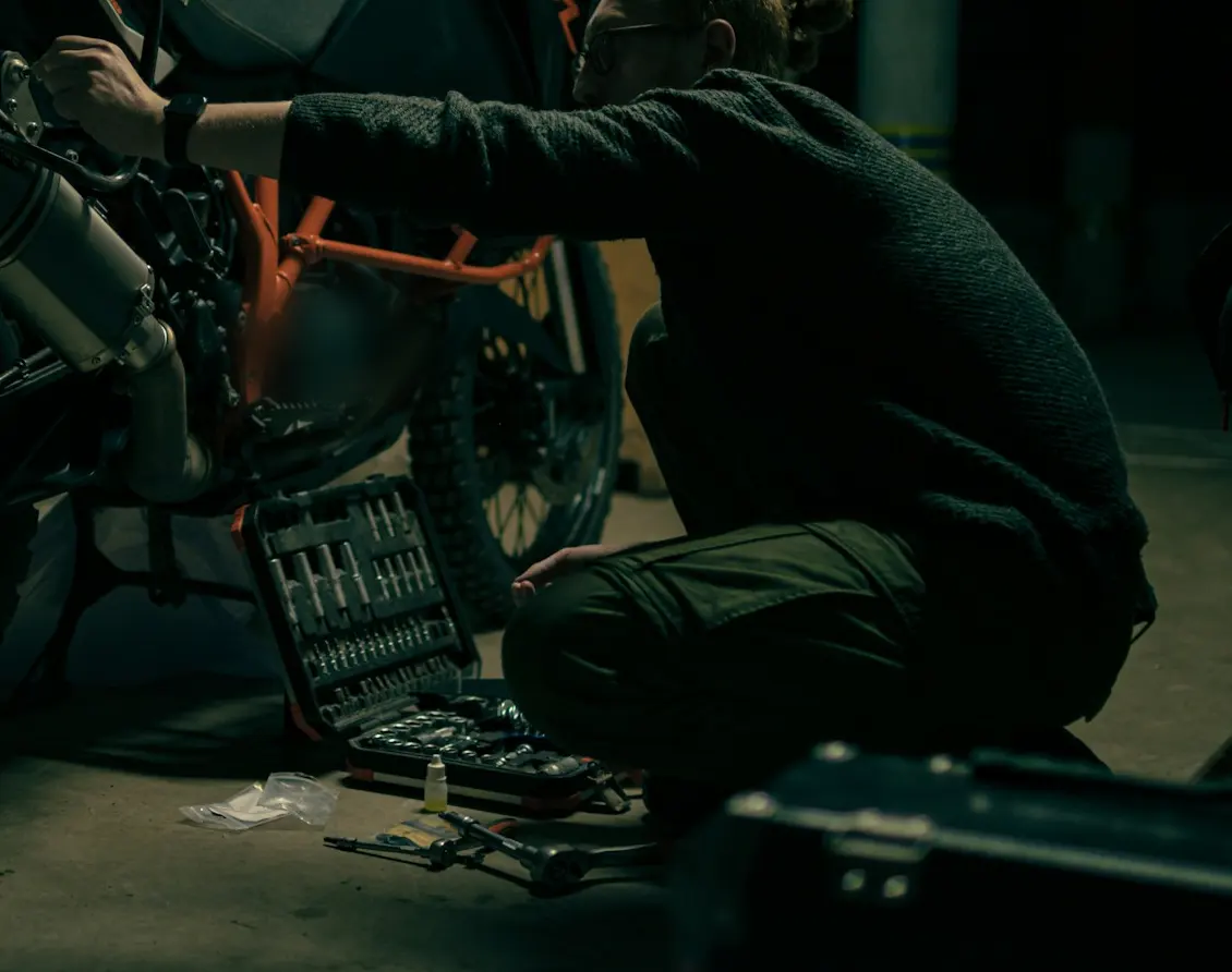 Technician crouching in an underground garage, tightening the exhaust mount of a motorcycle