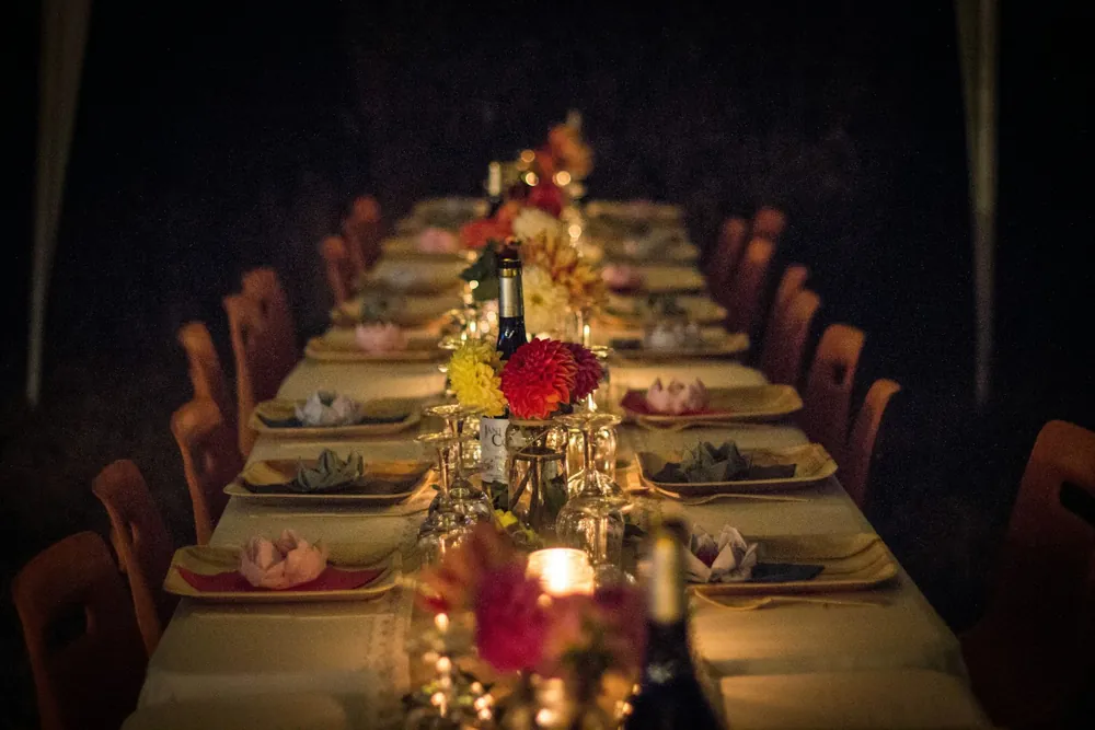 Long table in a dark room with red flowers and candles in glass hurricanes