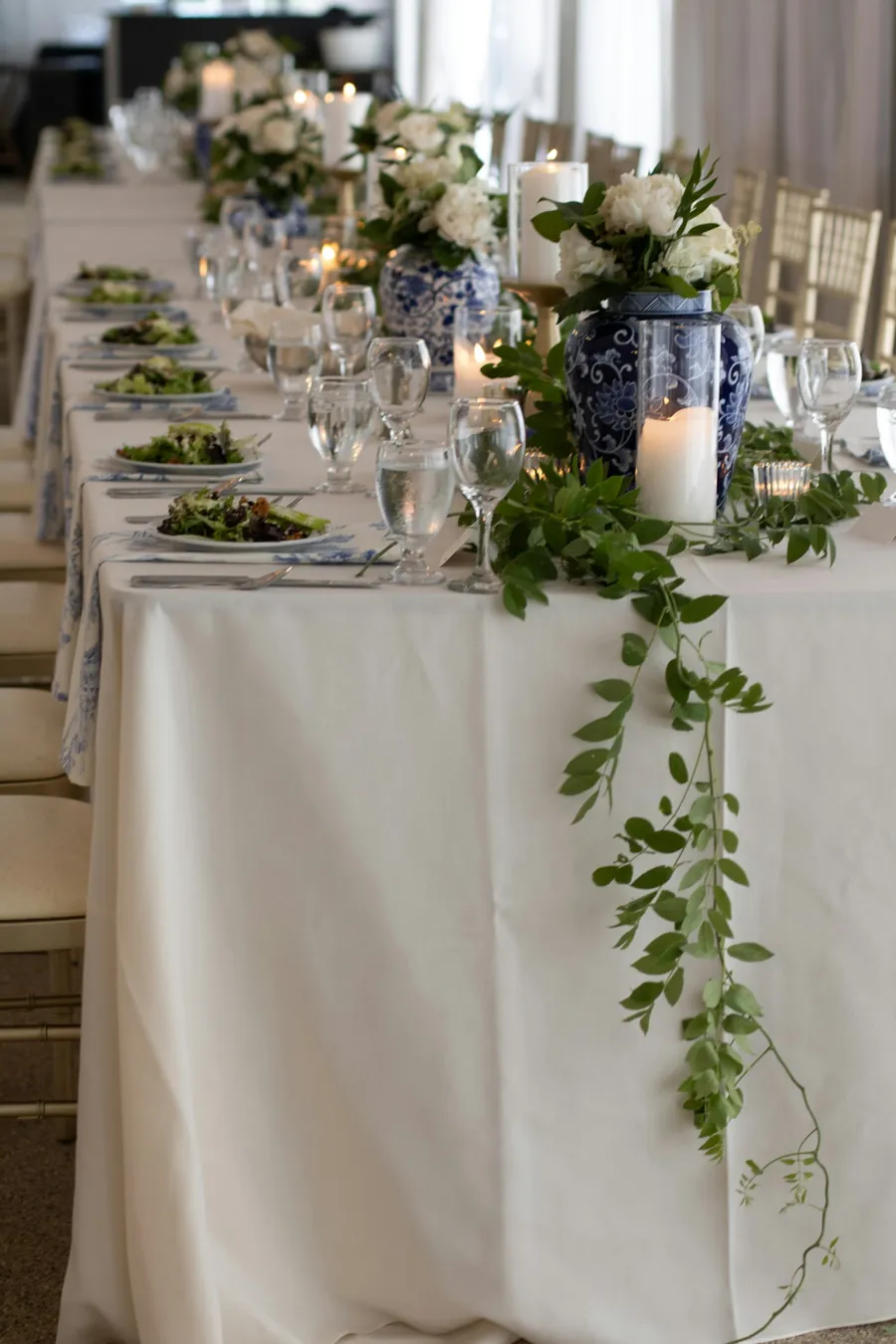 Long table with white roses, blue and white vases and ivy trailing from the tablecloth