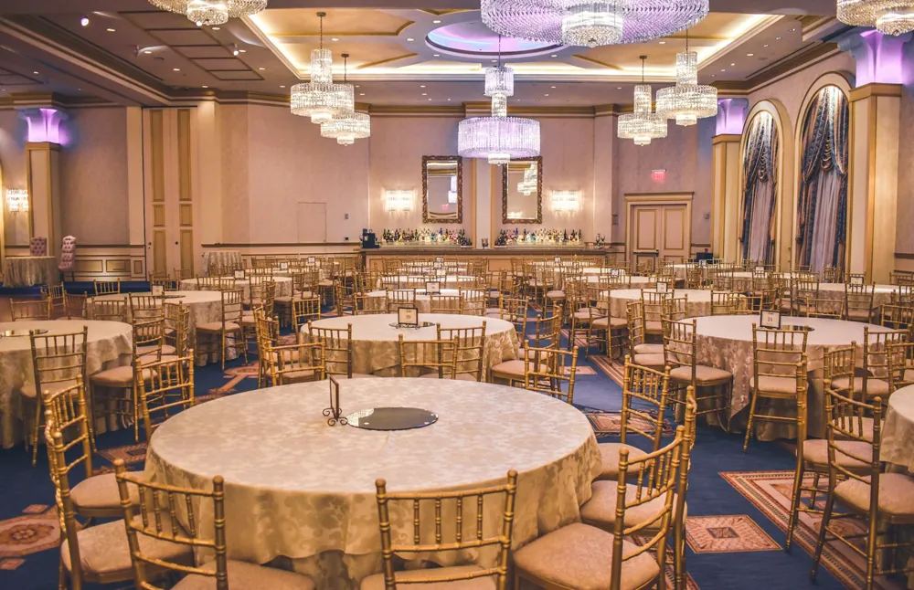Empty ballroom with chandeliers and round gala tables surrounded by gold chairs