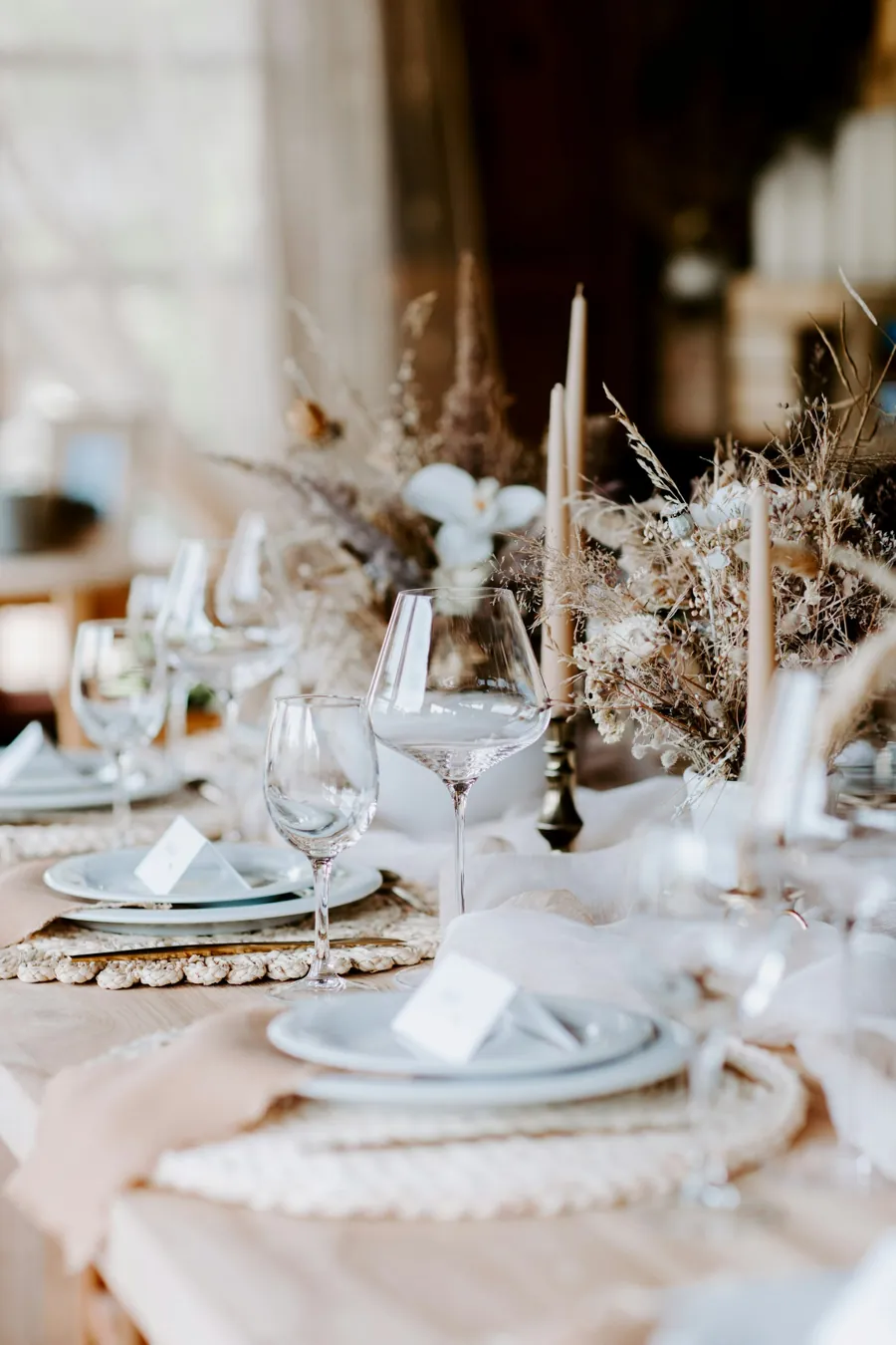 Table with dried flowers, beige taper candles, woven placemats and name cards