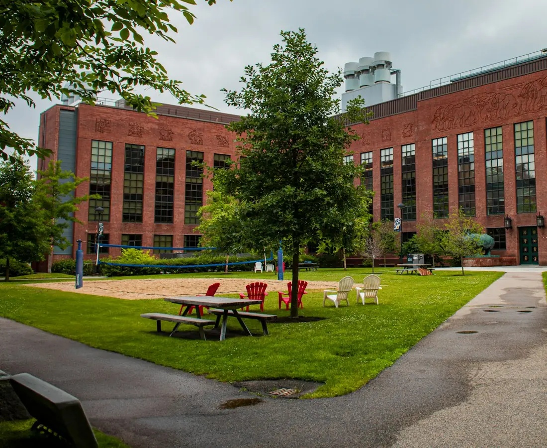 A brick school building behind a tree lined lawn with picnic tables