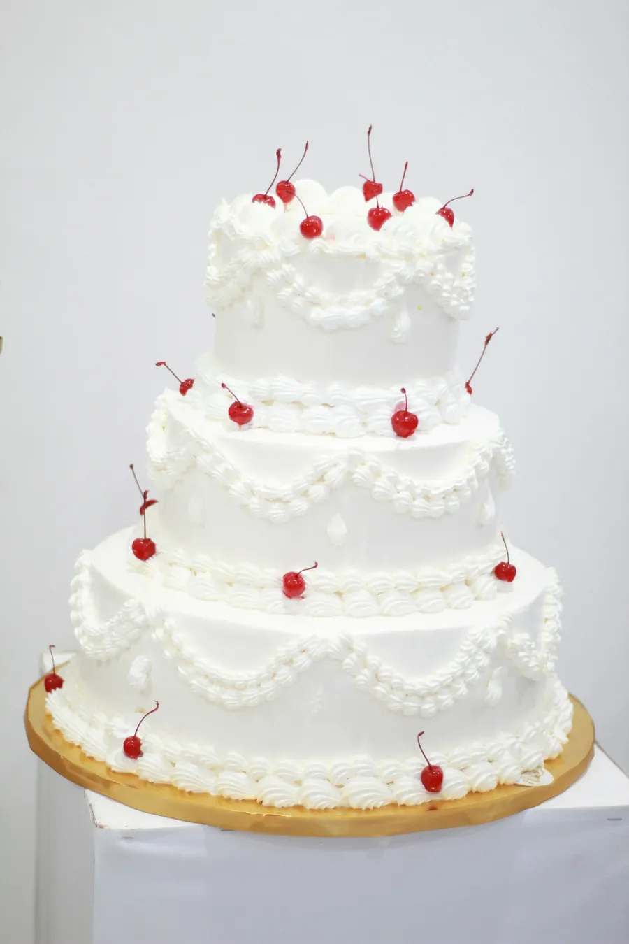 Three tier white wedding cake piped with cream and topped with cherries