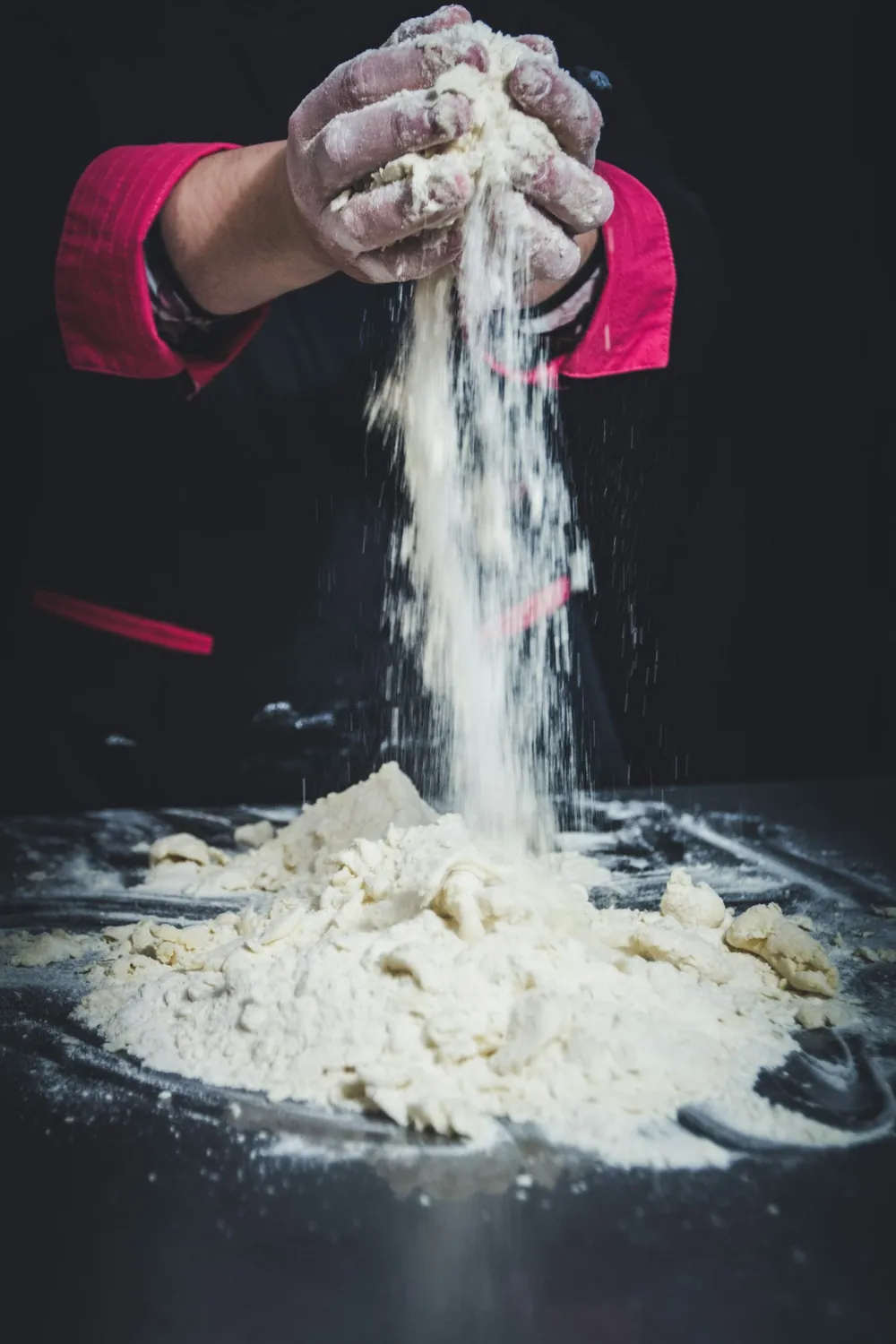 Floury hands sprinkling flour onto a dough bench