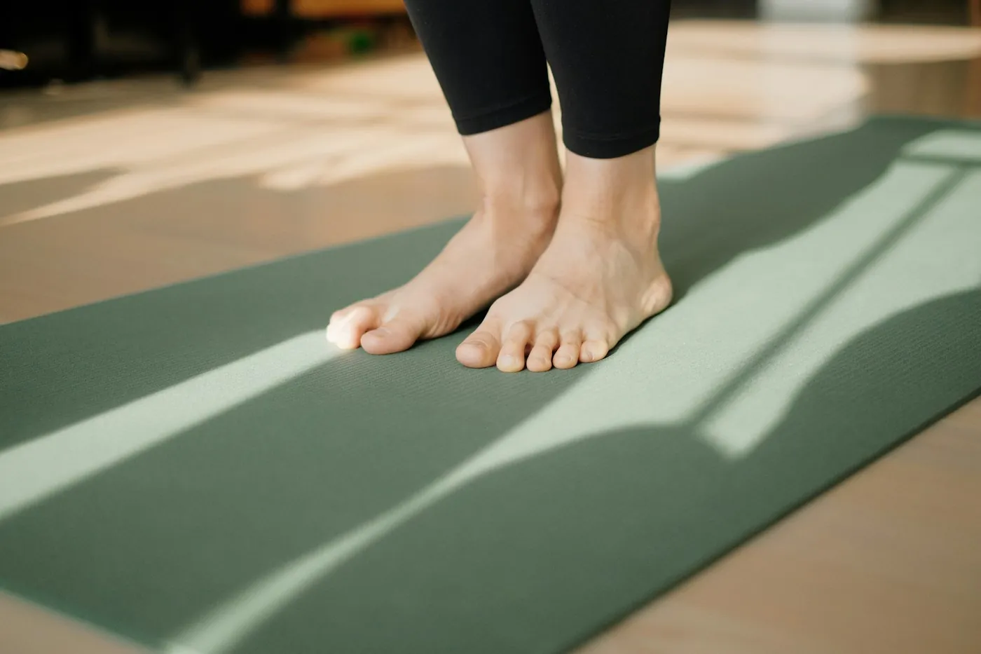 Bare feet on a green yoga mat crossed by sunlight