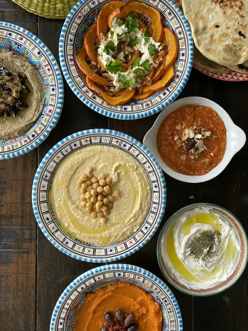 Overhead view of hummus, roasted squash and yoghurt mezze plates on a wooden table