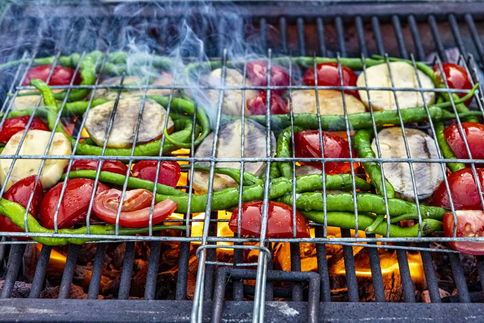 Aubergine, peppers, tomatoes and courgette on a grill rack over glowing embers