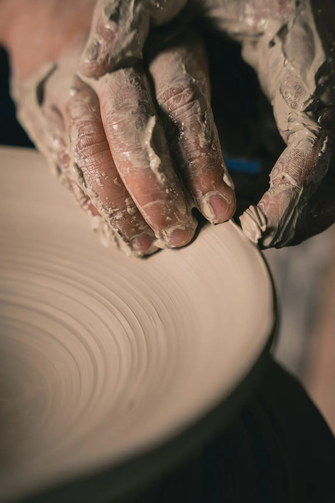 Close up of two clay covered hands on a spinning wheel