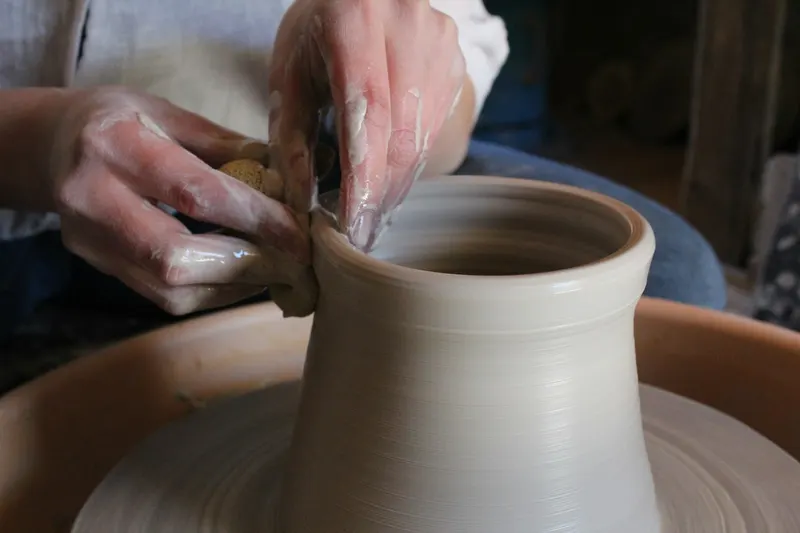 A pale vase rising on the wheel, shaped by two hands