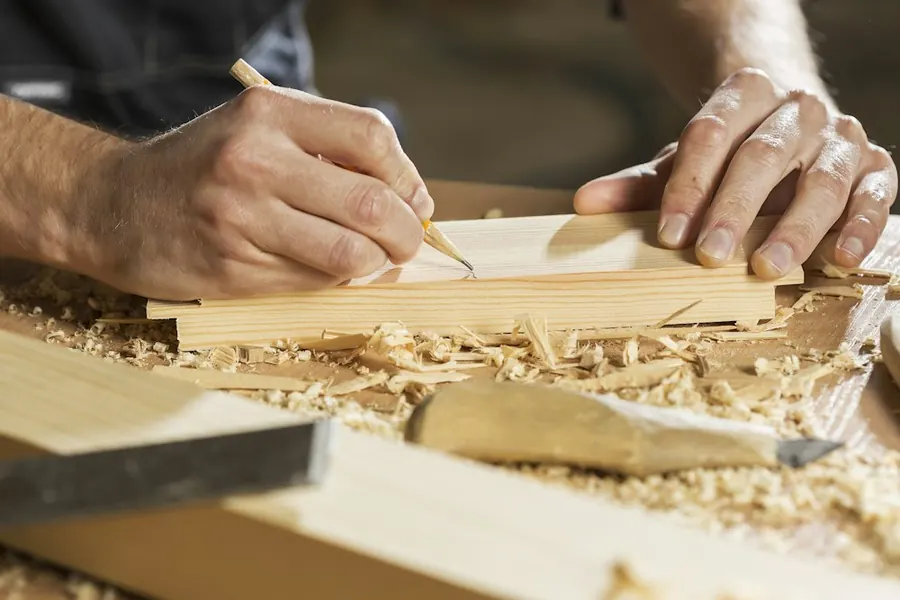 Hands marking measurements on a wooden board with a pencil