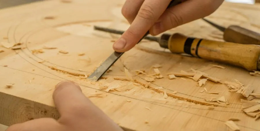 Hands carving a wooden surface with a chisel