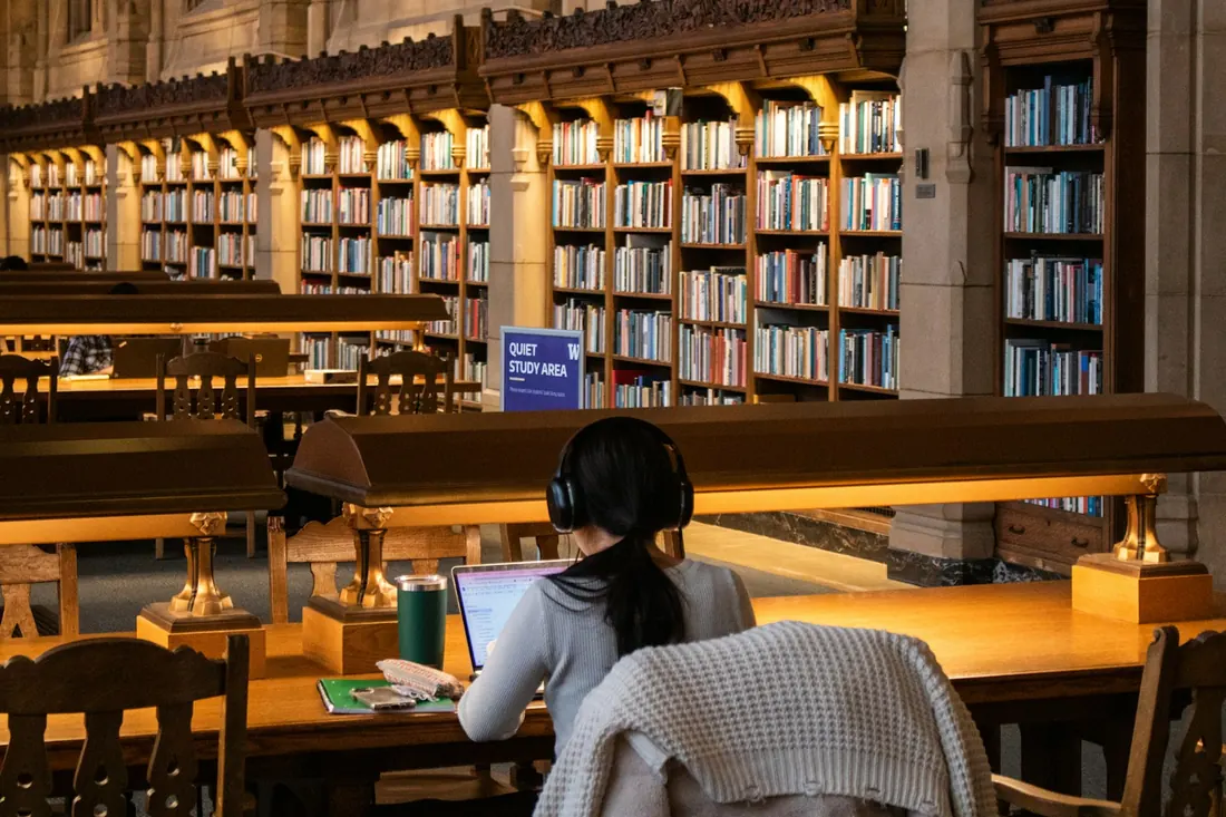 A student working on a laptop at a desk in a large library
